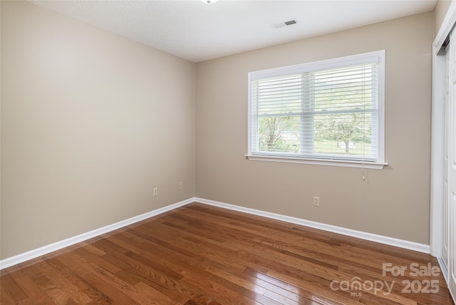 empty room with baseboards, visible vents, and wood finished floors