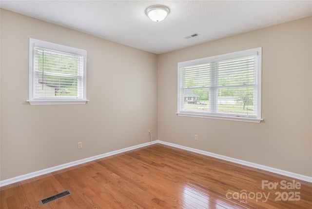 empty room with visible vents, a wealth of natural light, and light wood-type flooring