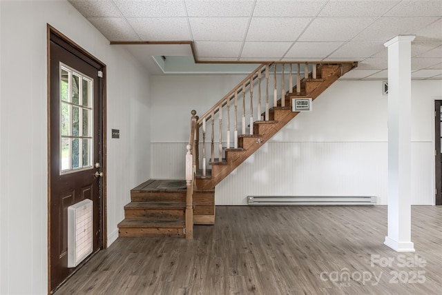 entryway with stairs, baseboard heating, a drop ceiling, and wood finished floors