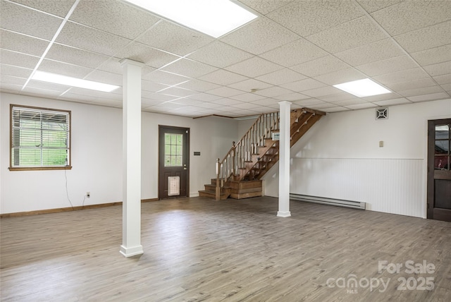 below grade area with stairs, a drop ceiling, wood finished floors, and a baseboard radiator