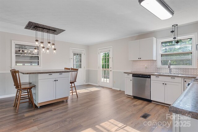 kitchen with a sink, a kitchen bar, tasteful backsplash, stainless steel dishwasher, and dark wood-style floors