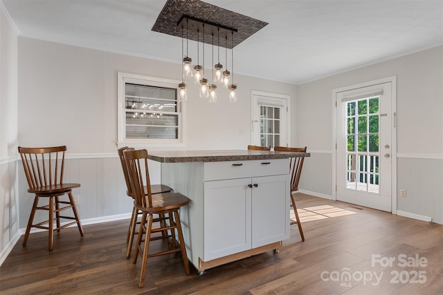 dining space featuring crown molding, a wainscoted wall, baseboards, and dark wood finished floors