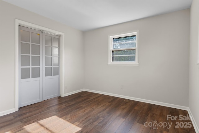unfurnished room featuring dark wood-style flooring, baseboards, and visible vents