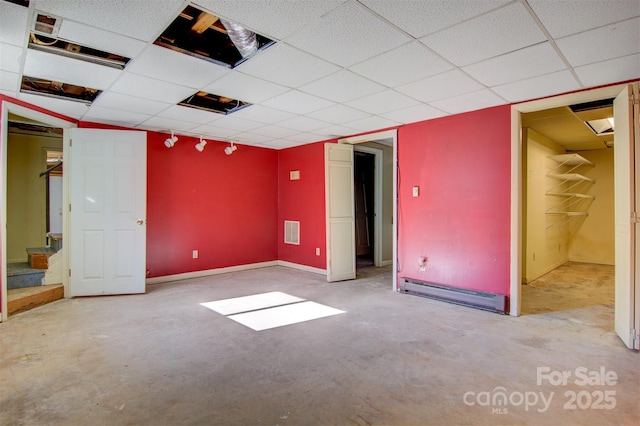 unfurnished bedroom with concrete flooring, a paneled ceiling, baseboards, a baseboard radiator, and visible vents