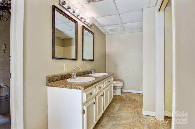 bathroom with double vanity, a sink, a drop ceiling, and toilet