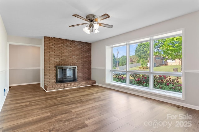 unfurnished living room with baseboards, ceiling fan, a fireplace, and wood finished floors