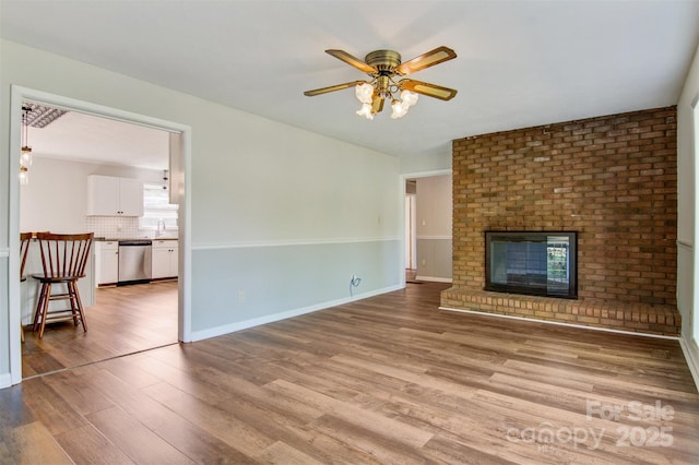 unfurnished living room featuring ceiling fan, a fireplace, wood finished floors, a sink, and baseboards