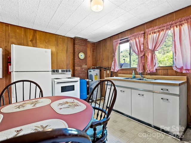 kitchen featuring wood walls, white cabinetry, white appliances, and a sink