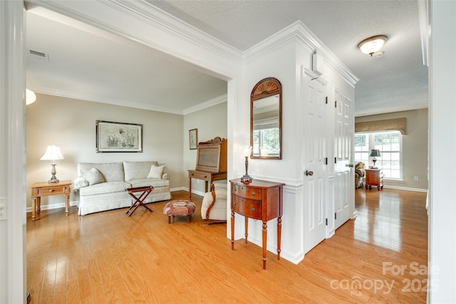 living area with baseboards, visible vents, light wood-style floors, and crown molding