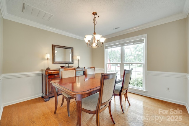 dining room with ornamental molding, visible vents, light wood-style flooring, and a notable chandelier