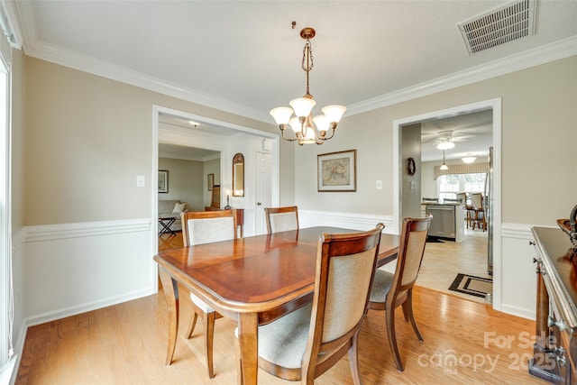 dining space featuring light wood-style floors, a notable chandelier, crown molding, visible vents, and wainscoting