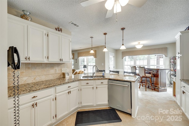 kitchen featuring a sink, decorative backsplash, a peninsula, stainless steel dishwasher, and white cabinets