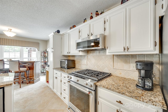 kitchen with light stone countertops, backsplash, a textured ceiling, white cabinets, and appliances with stainless steel finishes