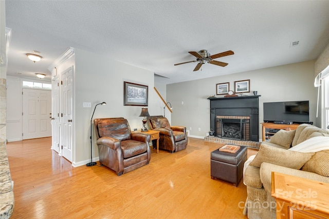 living area with stairway, light wood finished floors, a brick fireplace, visible vents, and a ceiling fan