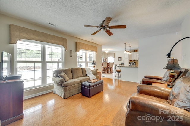 living area featuring a textured ceiling, visible vents, ceiling fan, and light wood-style floors