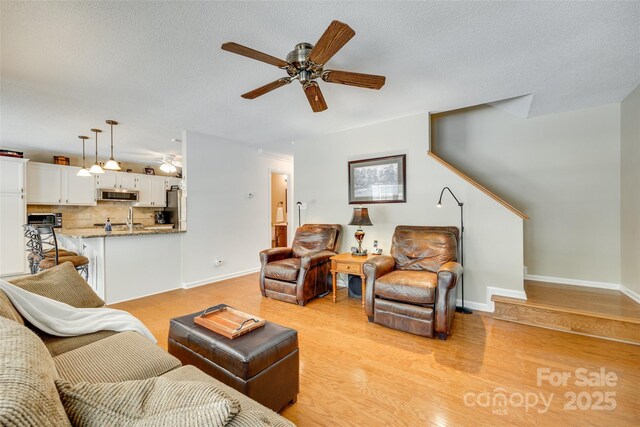 living area featuring a textured ceiling, light wood-type flooring, a ceiling fan, and baseboards