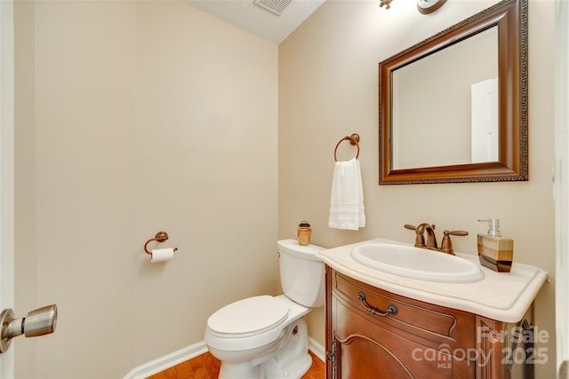 half bath featuring wood finished floors, toilet, vanity, baseboards, and visible vents