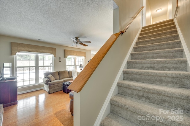 staircase featuring a textured ceiling, wood finished floors, and a wealth of natural light