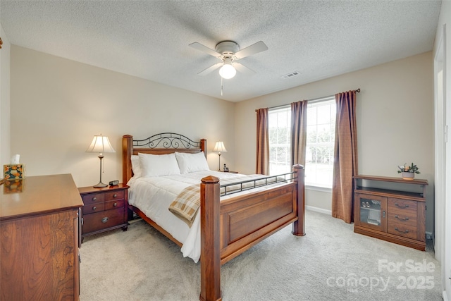 bedroom featuring ceiling fan, visible vents, light carpet, baseboards, and a textured ceiling