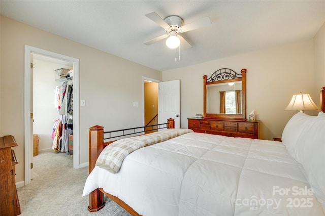 bedroom with baseboards, light colored carpet, a closet, ceiling fan, and a walk in closet