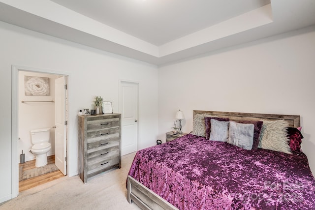 carpeted bedroom featuring ensuite bathroom and a raised ceiling