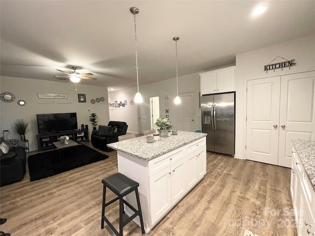 kitchen with open floor plan, ceiling fan, stainless steel fridge, white cabinets, and light wood-style flooring