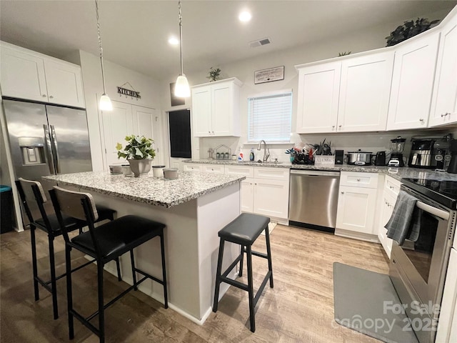 kitchen with appliances with stainless steel finishes, a sink, a kitchen breakfast bar, a center island, and visible vents