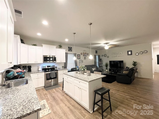 kitchen featuring open floor plan, ceiling fan, a center island, a sink, and appliances with stainless steel finishes