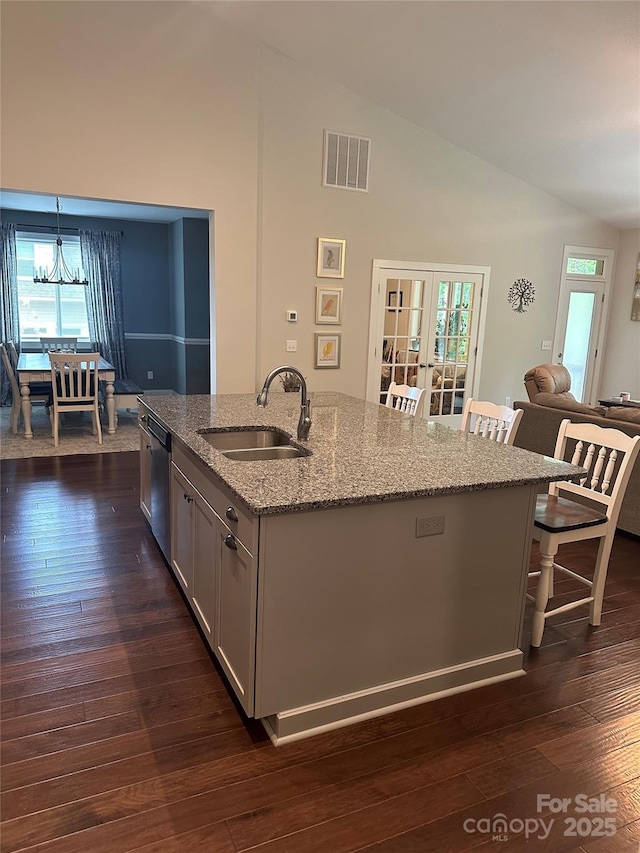 kitchen featuring light stone countertops, a kitchen island with sink, dishwasher, a sink, and visible vents