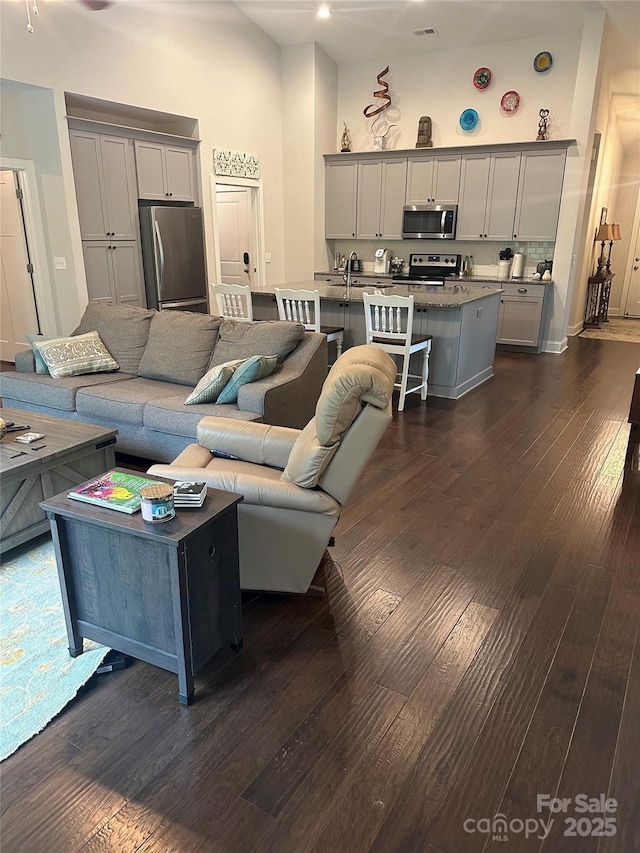 living room featuring a towering ceiling, dark wood-style flooring, and visible vents