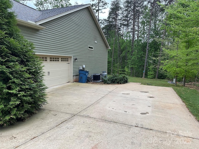 view of side of property featuring cooling unit, concrete driveway, an attached garage, and roof with shingles