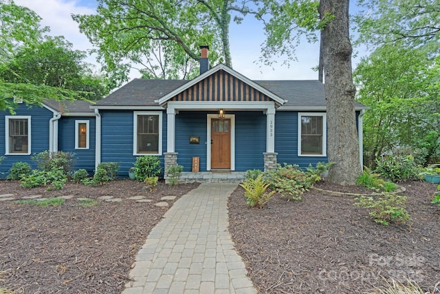 view of front of home with a chimney, a porch, board and batten siding, and roof with shingles