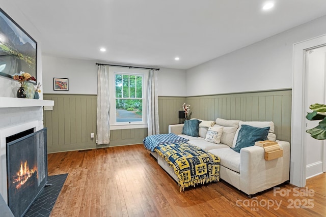 bedroom featuring a fireplace with flush hearth, wood finished floors, recessed lighting, and wainscoting