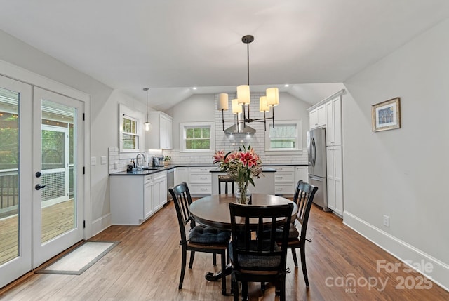 dining room with wood finished floors, an inviting chandelier, vaulted ceiling, baseboards, and french doors
