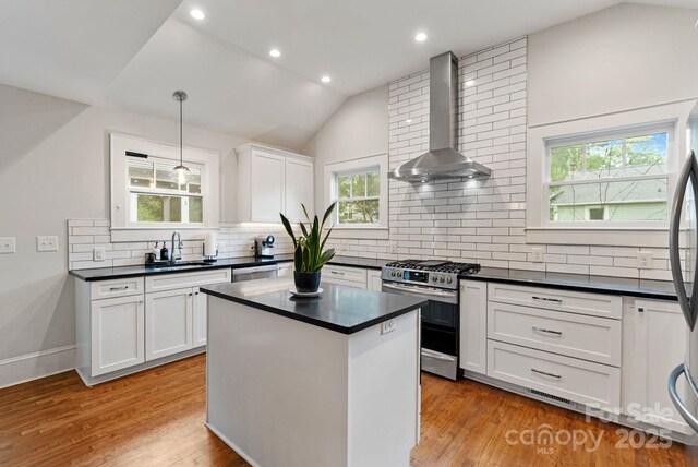 kitchen featuring gas stove, wall chimney range hood, dark countertops, a sink, and lofted ceiling