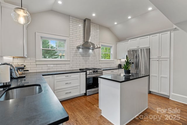 kitchen featuring appliances with stainless steel finishes, vaulted ceiling, dark countertops, a sink, and wall chimney exhaust hood