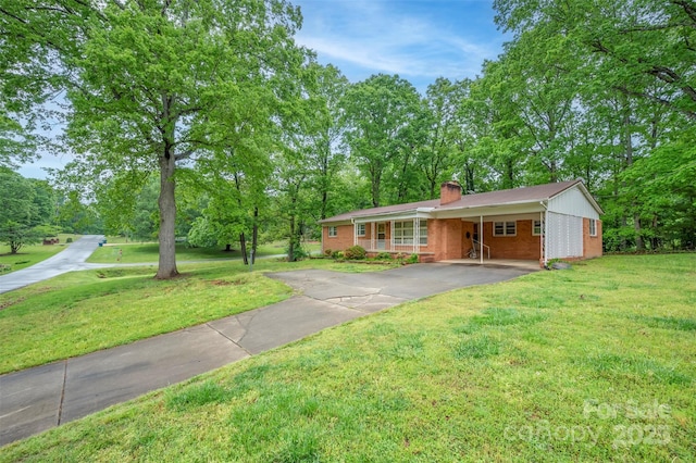 ranch-style home featuring aphalt driveway, brick siding, an attached carport, a front yard, and a chimney
