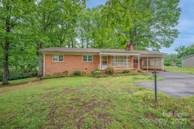 ranch-style home featuring covered porch, a chimney, a front yard, brick siding, and concrete driveway