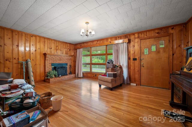 living area featuring light wood-style floors, wood walls, a brick fireplace, and a chandelier