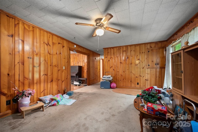 interior space featuring carpet flooring, ceiling fan, and wood walls