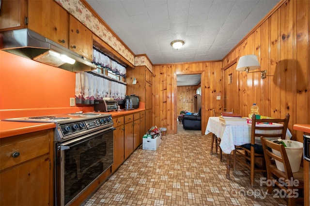 kitchen with under cabinet range hood, brown cabinets, wood walls, and range with electric stovetop