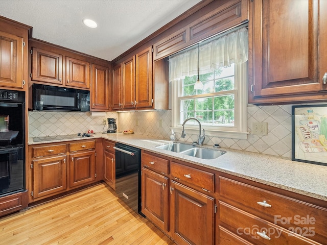 kitchen with black appliances, light wood-type flooring, decorative backsplash, and a sink