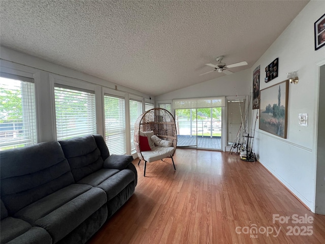 living room featuring ceiling fan, vaulted ceiling, light wood finished floors, and a textured ceiling