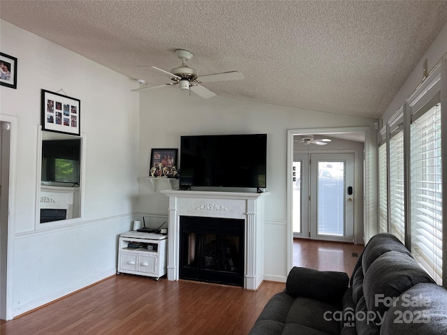 living room with a ceiling fan, a textured ceiling, a fireplace, wood finished floors, and lofted ceiling