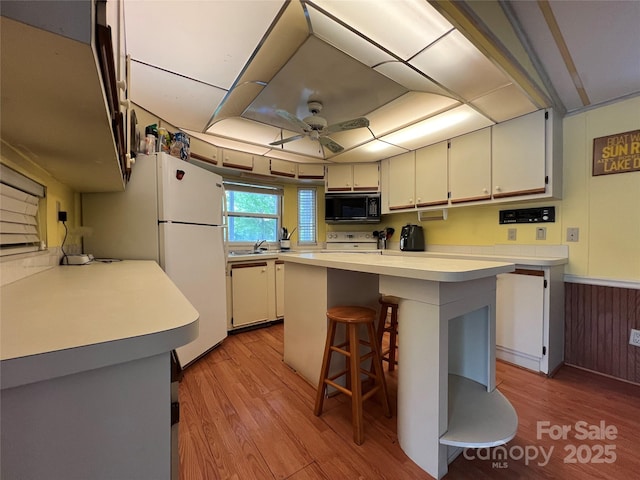 kitchen with ceiling fan, a kitchen bar, light countertops, light wood finished floors, and white appliances