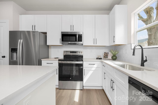 kitchen with appliances with stainless steel finishes, white cabinetry, light wood finished floors, and a sink