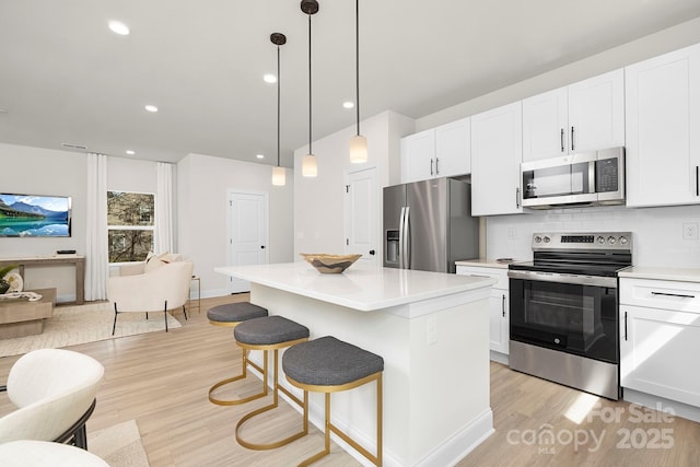 kitchen with appliances with stainless steel finishes, light countertops, white cabinets, light wood finished floors, and open floor plan