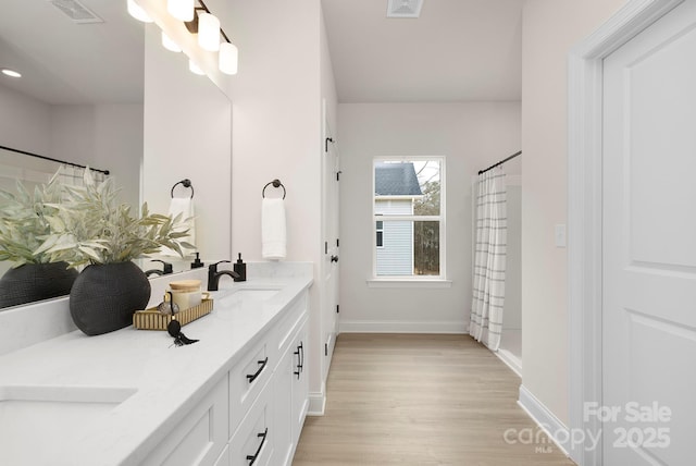 bathroom with wood finished floors, double vanity, a sink, baseboards, and visible vents