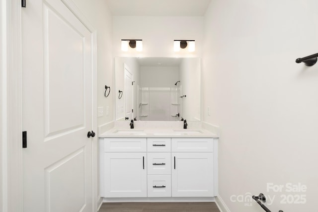 full bathroom featuring double vanity, wood finished floors, walk in shower, and a sink