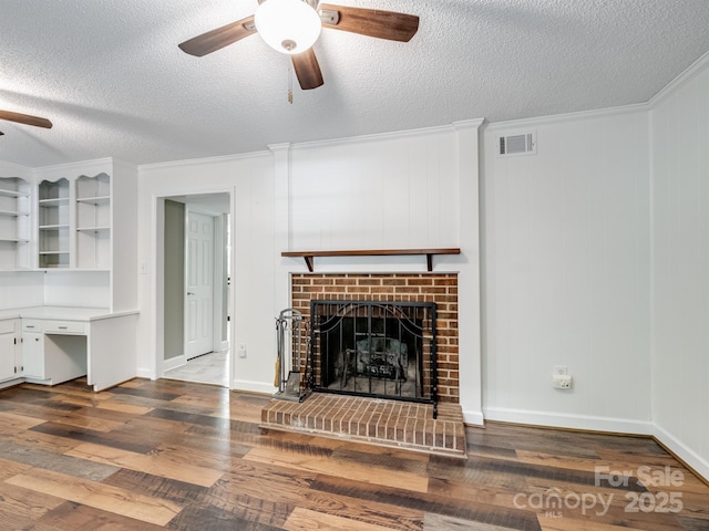 unfurnished living room featuring ceiling fan, a brick fireplace, a textured ceiling, wood finished floors, and ornamental molding